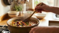 Person stirring colorful vegetable soup in rustic bowl with wooden spoon in cozy kitchen setting for healthy cooking and meal preparation.
