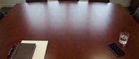 Young professional male of mixed ethnicity sitting at polished wooden conference table with notebook, pen, and smartphone, ready for business meeting or corporate discussion.