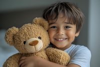 Young boy with bright smile hugging large brown teddy bear, showing childhood joy and innocence against blurred background. Close up portrait capturing pure happiness.