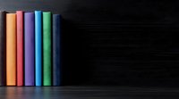 Colorful hardcover books standing in row against dark background, creating minimalist composition with vibrant spines in orange, purple, green and blue tones.