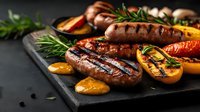 Grilled sausages with charred orange slices and fresh rosemary on black stone board. Juicy meat with grill marks and caramelized citrus creates appetizing composition.