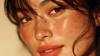 Young woman with freckles and wet hair in golden sunlight. Natural beauty portrait with warm lighting for skincare, cosmetics and wellness campaigns.