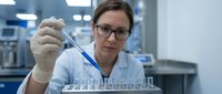 Female scientist in white lab coat and safety glasses using pipette for precise liquid measurement in modern laboratory research facility.