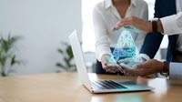 Diverse business professionals collaborating over digital hologram pyramid at wooden desk with laptop, representing teamwork, innovation, and data analysis in modern office environment.