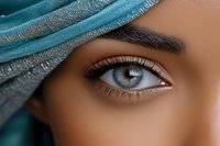 Close up view of expressive blue eye with long eyelashes and defined eyebrow partially covered by turquoise fabric, representing beauty and mystery in middle eastern style.
