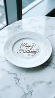 Elegant white ceramic plate with Happy Birthday script and silver glitter rim on a marble table, perfect for celebration and party concepts.