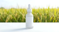White dropper bottle with pipette on clean surface against blurred green plant background for natural skincare and wellness product packaging mockup.