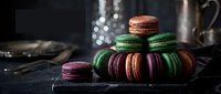 Colorful French macarons stacked on dark slate surface with elegant bokeh lighting creating luxurious dessert display for bakery and confectionery marketing.