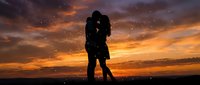 Silhouette of couple kissing against dramatic golden sunset sky with sparkling lights, romantic evening scene for love and relationships.