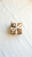 Kraft paper gift box with cream ribbon bow and eucalyptus leaves on white linen fabric background, suitable for holiday packaging and greeting card designs.
