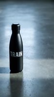 Black insulated water bottle with motivational text on concrete surface with moody blue-toned background, suitable for fitness, wellness, and lifestyle marketing campaigns.