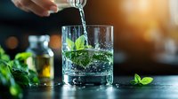 Fresh mint leaves splash in crystal glass with pouring water, ice cubes and bubbles on dark background with bokeh lights. Refreshing summer drink concept.