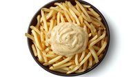 Golden french fries served in dark ceramic bowl with creamy sauce dollop in center, shot from above on white background, isolated for menu and food service.