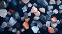 Colorful sea glass pieces scattered on dark background, featuring pink, white, and navy blue frosted fragments in artistic arrangement for decorative design.