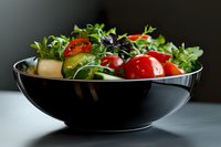 Fresh mixed salad with cherry tomatoes, cucumber, and arugula served in modern black ceramic bowl against dark background. Healthy eating concept.