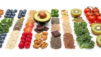 Healthy superfood selection with fresh fruits, vegetables, nuts, seeds and grains arranged in colorful rows on white background for nutritious diet planning.