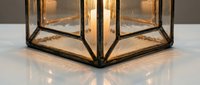 Geometric brass and glass lantern with warm interior lighting casting reflections on white surface, suitable for home decor and interior design projects.