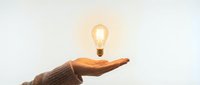 Glowing light bulb floating above open palm of hand in sweater against neutral background symbolizing innovation, creativity and bright ideas for business concepts.