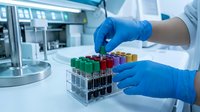 Scientist in blue latex gloves holding test tube with red liquid in laboratory rack, conducting chemical or medical research analysis in modern clinical facility.