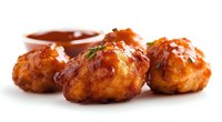 Crispy chicken meatballs glazed with spicy buffalo sauce and fresh herbs, served with dipping sauce on white background, close up view for menu and recipe content.