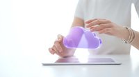 Hands holding glowing purple cloud symbol above digital tablet representing cloud computing technology and data storage solutions for modern business.