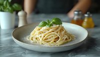 Classic spaghetti pasta with parmesan cheese and fresh basil leaf served on ceramic plate against marble table background in restaurant setting.