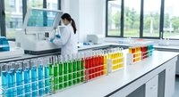Colorful test tubes with chemical solutions arranged in laboratory rack while female scientist works in modern research facility background.