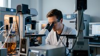 Male scientist examining samples through microscope in modern laboratory conducting research and analysis for medical or scientific discovery.