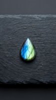 Labradorite gemstone with blue and green flash on dark slate surface displaying natural iridescent colors and mineral crystal formation for jewelry design.