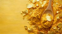 Golden turmeric powder scattered on yellow surface with wooden spoon, bright aromatic spice ingredient for cooking and wellness, top view with copy space.