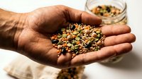 Handful of mixed legumes and seeds held by a male hand, showcasing colorful lentils, beans, and grains for healthy nutrition concepts.