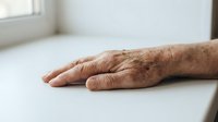 Elderly male hands with age spots and wrinkles resting on white surface, showing mature skin texture and aging signs for healthcare and wellness content.