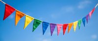 Colorful rainbow bunting flags strung across clear blue sky with white clouds, perfect for celebrations, parties, festivals, and festive event decorations.