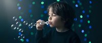 Young child blowing soap bubbles against colorful bokeh lights background creating magical childhood moment for family and lifestyle concepts.