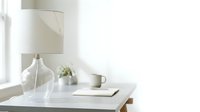 Minimalist workspace with clear glass vase, white mug, notebook and small potted plant on marble table near window with natural light.