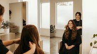 Professional hair stylist working with female client in modern salon interior with natural lighting and minimalist design for beauty services.