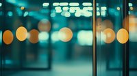 Blurred city lights create dreamy bokeh effect in teal and gold tones through glass window, modern urban nighttime atmosphere for backgrounds and mood designs.