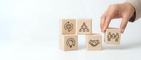 Business strategy concept with hand placing wooden blocks featuring corporate icons including teamwork, leadership, innovation and partnership symbols.