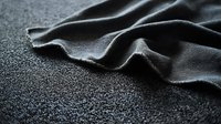 Soft black fabric with gentle folds and waves creates dramatic shadows against textured dark background, showcasing luxurious textile material for fashion and design projects.