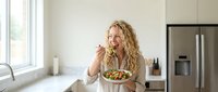 Young blonde Caucasian woman enjoying healthy salad in modern kitchen. Lifestyle concept for nutrition, wellness, and home cooking habits.