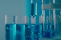 Close-up of laboratory dropper dispensing blue liquid into test tubes filled with chemical solutions for scientific research and medical testing.