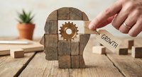 Business growth mindset concept with wooden puzzle head, gear mechanism and hand holding growth key for personal development and success strategies.