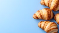 Fresh baked golden croissants arranged on light blue background with copy space. French pastry breakfast composition for bakery menu or food design.
