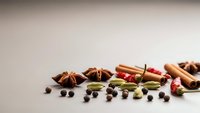 Aromatic spices and herbs scattered on neutral background including cinnamon sticks, star anise, cardamom pods, peppercorns for culinary cooking.