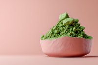 Green matcha tea powder in pink ceramic bowl against pastel pink background, minimalist food photography composition for wellness and lifestyle content.