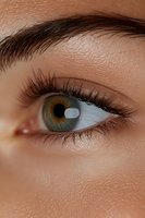 Close-up macro shot of green eye with long eyelashes and defined eyebrow showing natural skin texture and pores. For beauty, cosmetic, and medical concepts.