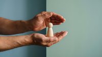Male hands protecting wooden figure person symbolizing care, support and human resources management concept for business presentations.