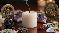 Mystical altar setup with burning candle, amethyst crystals, tarot cards, skull and spiritual symbols for meditation and divination practices.