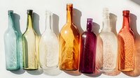 Vintage glass bottles in different colors casting shadows on white surface. Decorative arrangement shows textured designs and embossed patterns.