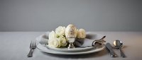 Elegant table setting with white roses and golden egg in silver holder, fine dining arrangement with cutlery on neutral background for luxury events.